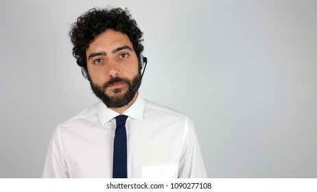 Handsome Consultant Of Call Center In Headphones On Gray Background. Young And Brunette Man Looking Serious At Camera.
