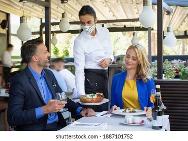 Handsome Couple Having Lunch In The Restaurant, Being Served By A Waitress With A Mask, Coronavirus Time