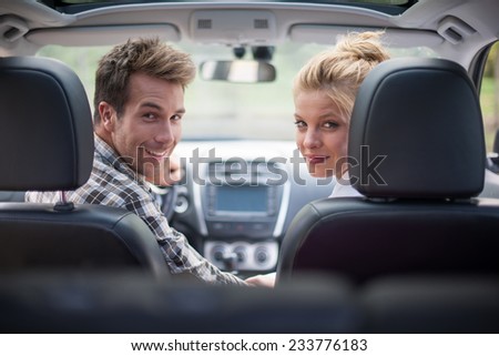 handsome couple looking at camera sitting in a car, view from rear seat