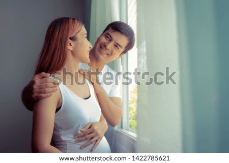 Handsome couples and pregnant moms in the romantic atmosphere while standing near the window at home
