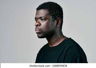 Handsome Curly Black Man In A T-shirt On A Gray Background Side View                              