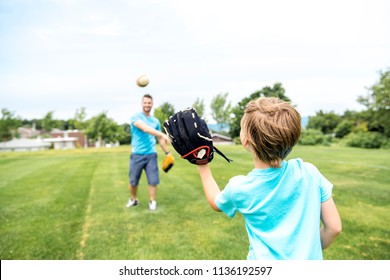 Handsome dad with his little cute sun are playing baseball on green grassy lawn