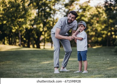 Handsome Dad With His Little Cute Sun Are Playing Baseball On Green Grass Lawn