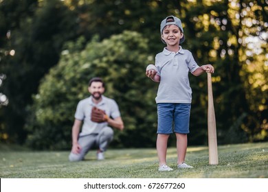 Handsome Dad With His Little Cute Sun Are Playing Baseball On Green Grassy Lawn