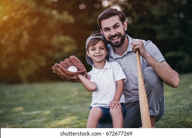 Handsome Dad With His Little Cute Sun Are Playing Baseball On Green Grassy Lawn