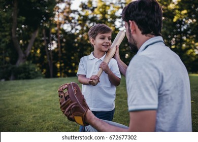Handsome dad with his little cute sun are playing baseball on green grass lawn
