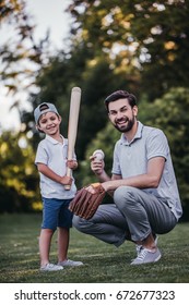 Handsome Dad With His Little Cute Sun Are Playing Baseball On Green Grassy Lawn