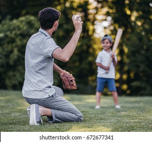 Handsome Dad With His Little Cute Sun Are Playing Baseball On Green Grassy Lawn