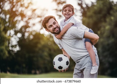 Handsome dad with his little cute sun are having fun and playing football on green grassy lawn