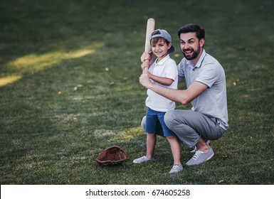 Handsome Dad With His Little Cute Sun Are Playing Baseball On Green Grassy Lawn