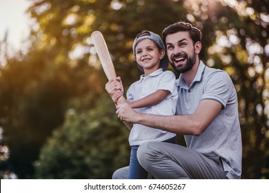 Handsome Dad With His Little Cute Sun Are Playing Baseball On Green Grassy Lawn