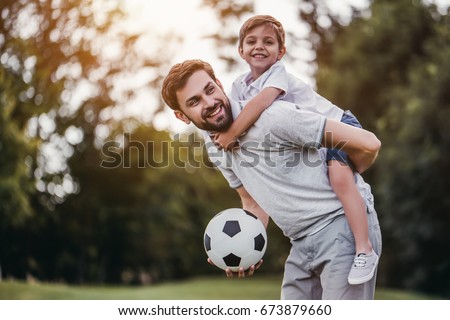 Handsome dad with his little cute sun are having fun and playing football on green grassy lawn