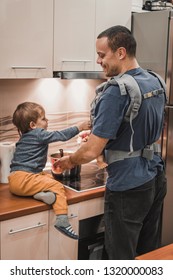 Handsome Dad In Kitchen With Child And Baby Carrier. Father With Newborn And Child Boy At Home In Kitchen Cooking 