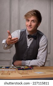 Handsome  Dealer  Inviting For Game Showing Chips Near Table With  Red Blue And White Chips In Piles In Casino