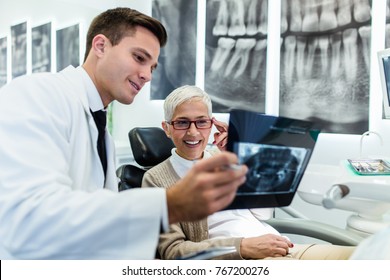 Handsome Dentist Looking At X-ray Image Of His Senior Woman Patient. 