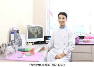 Handsome Dentist Sitting On Computer Desk With His Hand Read Document, Smile And Looking At Camera, Trust Responsibility Healthcare Staff In Smart Technology Hospital Concept.