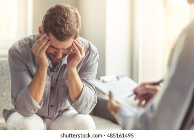 Handsome Depressed Man In Casual Clothes Is Leaning On His Knees, Crying And Telling About His Problems While Sitting On The Couch At The Psychotherapist