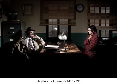 Handsome Detective At Office Desk Interviewing A Young Woman, 1950s Film Noir Style.