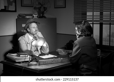 Handsome Detective At Office Desk Interviewing A Young Woman, 1950s Film Noir Style.