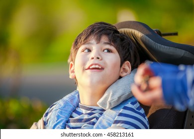 Handsome disabled nine year old boy sitting in wheelchair outdoors looking up into sky  - Powered by Shutterstock