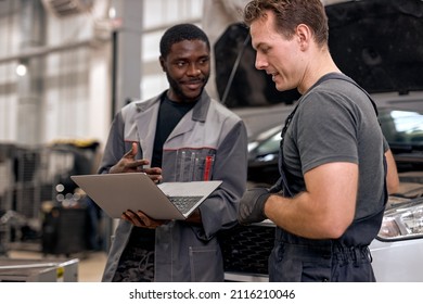 Handsome diverse mechanics in uniform examining car, using laptop while working in auto service. black and caucasian Auto mechanics checking car,service via online insurance system at garage - Powered by Shutterstock