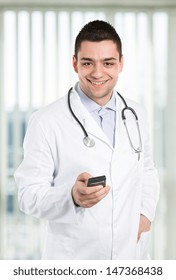 Handsome Doctor Holding Cell Phone At The Office.