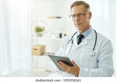Handsome doctor in lab coat using tablet computer in clinic