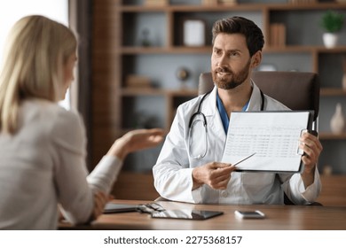 Handsome Doctor Man Showing Medical Test Results To Female Patient During Meeting In Clinic Office, Smiling Male Physician In Uniform Demonstrating Clipboard With Check Up Information To Young Woman - Shutterstock ID 2275368157