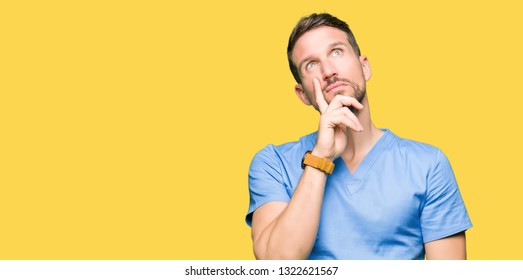 Handsome doctor man wearing medical uniform over isolated background with hand on chin thinking about question, pensive expression. Smiling with thoughtful face. Doubt concept.