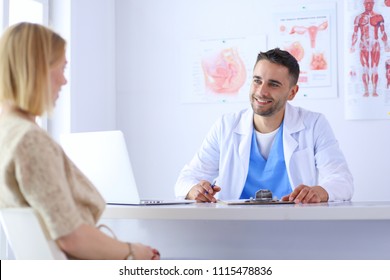 Handsome Doctor Is Talking With Young Female Patient And Making Notes While Sitting In His Office