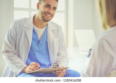 Handsome doctor is talking with young female patient and making notes while sitting in his office - Shutterstock ID 1183416208