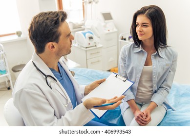 Handsome Doctor Is Talking With Young Female Patient And Making Notes While Sitting In His Office