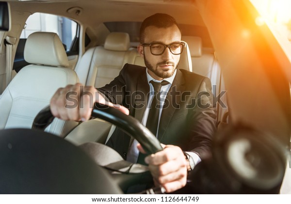 handsome driver in suit and glasses driving auto\
during sunset