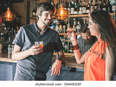 Handsome Drunk Man Sitting At Bar, Drinking Cocktail And Looking At Two Attractive Girls. He Wants To Get To Know Them, But Does Not Know How. Nightclub. Date