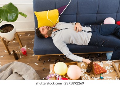 Handsome drunk man sleeping on the couch unconscious after drinking a lot of alcohol while celebrating a birthday party