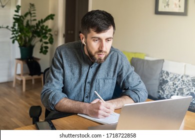 Handsome Eastern European Man Studying Remotely At Home During Corona Virus Quarantine Lockdown, Writing Down During Online Courses