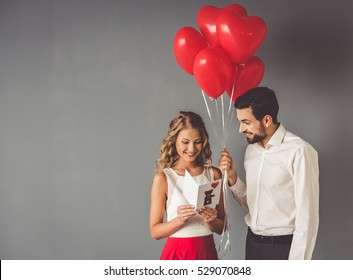 Handsome elegant guy is presenting a gift card and balloons to his beautiful girlfriend and smiling