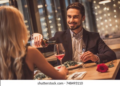 Handsome Elegant Man Is Looking At His Girlfriend, Pouring Wine And Smiling While They Having A Date In Restaurant