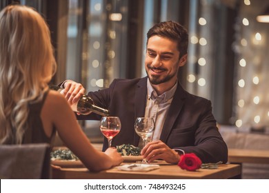 Handsome Elegant Man Is Pouring Wine And Smiling While Having A Date With His Girlfriend In Restaurant