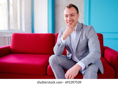 Handsome And Elegant Young Man Sitting On The Red Couch.