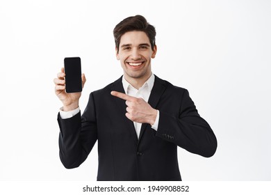 Handsome entrepreneur pointing at empty phone screen wth pleased, confident face, recommending an app or website, standing over white background - Powered by Shutterstock