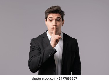 Handsome european brunette businessman with gesture of shhh, secret, silence, conspiracy, gossip concept. Smiling boss leader man holding finger on lips, white studio background. High quality