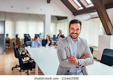 Handsome executive smiling in the office, with colleagues in background.  - Shutterstock ID 1116615500
