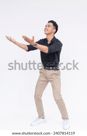 Handsome and fashionably cool Filipino man anticipating to catch something or someone falling down, extending his hands to the left. Full body photo, isolated on a white background.