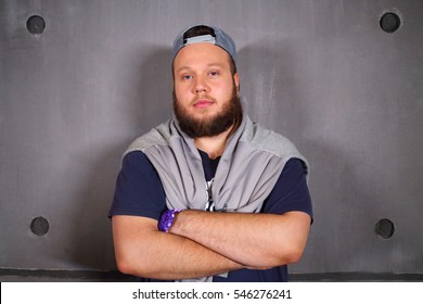 Handsome fat man with beard poses with crossed arms in studio near wall