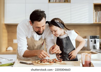 Handsome father with beared taking cheese from homemade pizza tasting. Curious daughter waiting for eating tasting delicious flavour of homemade pizza. - Powered by Shutterstock