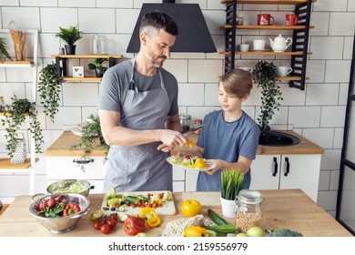 Handsome Father And His Teenager Son Spending Quality Time Together. Men Doing Chores, Cooking Healthy Vegetable Salad, Tasty Food In The Kitchen At Home