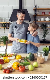 Handsome Father And His Teenager Son Spending Quality Time Together. Men Doing Chores, Cooking Healthy Vegetable Salad, Tasty Food In The Kitchen At Home