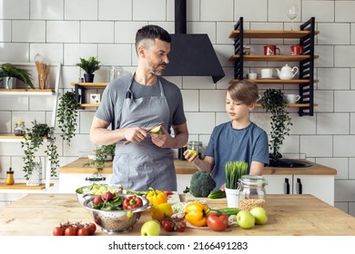 Handsome Father And His Teenager Son Spending Quality Time Together. Men Doing Chores, Cooking Healthy Vegetable Salad, Tasty Food In The Kitchen At Home