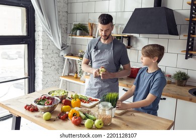 Handsome Father And His Teenager Son Spending Quality Time Together. Men Doing Chores, Cooking Healthy Vegetable Salad, Tasty Food In The Kitchen At Home